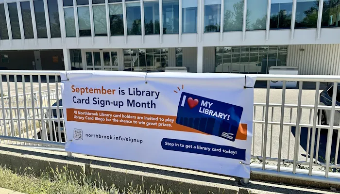 A photo of a banner on the library fence to celebrate Library Card Sign-up Month