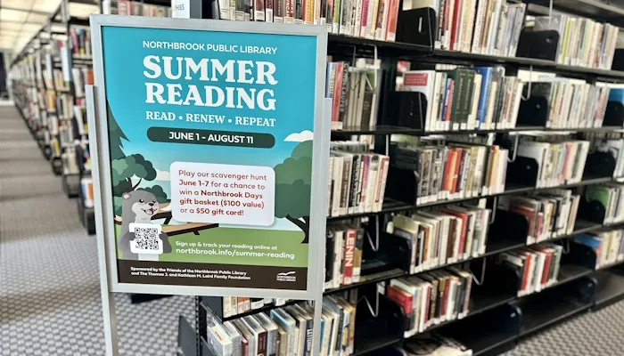 The Summer Reading poster in front of a library shelf full of books